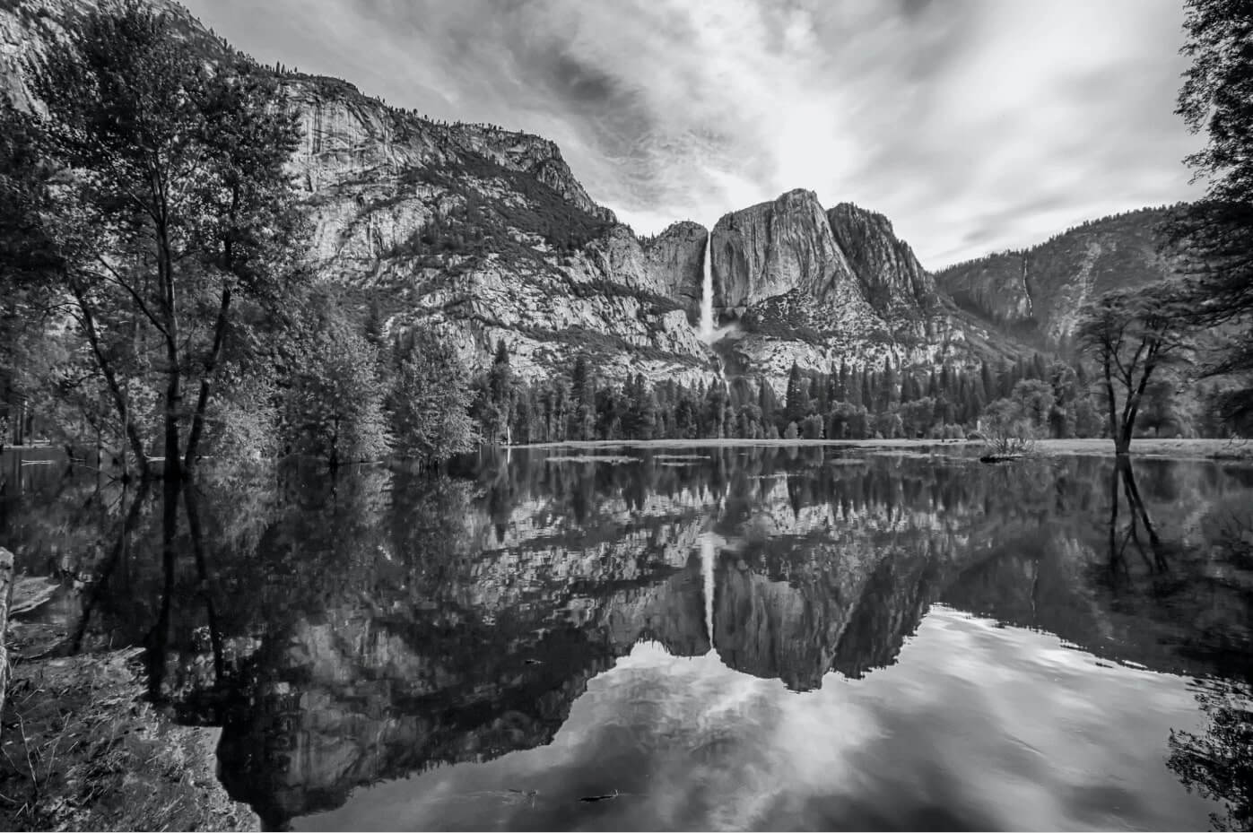 a black and white image of mountains with a lake in the foreground.